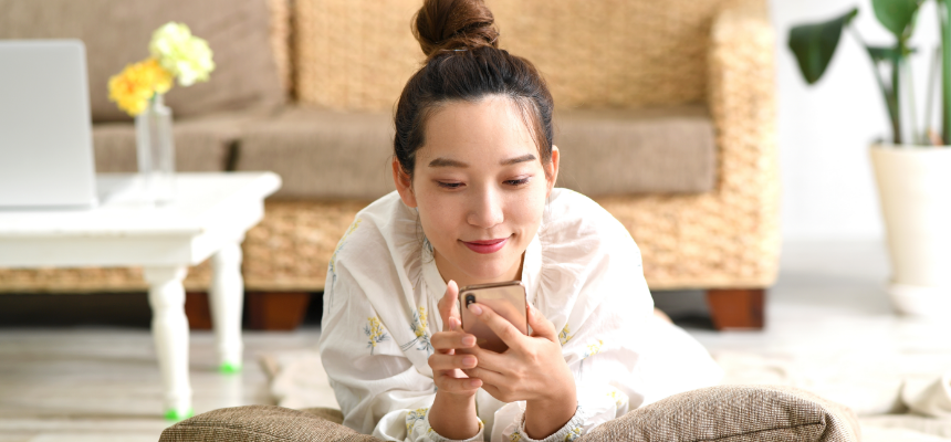 ソファの前で床に寝転びながらスマートフォンを見ている女性